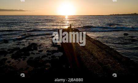 La gente si rilassa e si ammira seduti su un molo di pietra con l'oceano e il cielo del tramonto sullo sfondo. Concetto di gente serena e natura. Tempo libero all'aperto zen Foto Stock