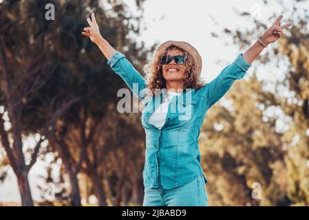 Persone allegre donna felice alzando le braccia con gesto di vittoria e sorridendo con alberi verdi natura sfondo. Ragazza allegra in Foto Stock
