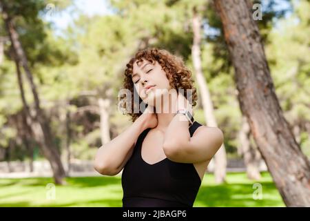 Bella donna rossa che indossa abiti sportivi in piedi sul parco cittadino, relax all'aperto con gli occhi chiusi, sensazione di vita, respirazione, sognare. Foto Stock