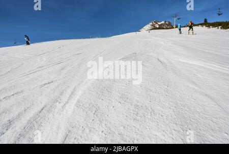 Pendio coperto di neve cristallina, pochi sentieri da sci visibile, sciatori sfocati e chiaro cielo sfondo blu Foto Stock