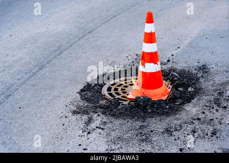 segnalare il cono di traffico su una botola fognaria difettosa su un'autostrada urbana Foto Stock