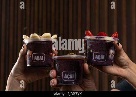Mix di deliziosa Açaí crema brasiliana, in una tazza di plastica con una varietà di condimenti. Frullato estivo di acai Foto Stock