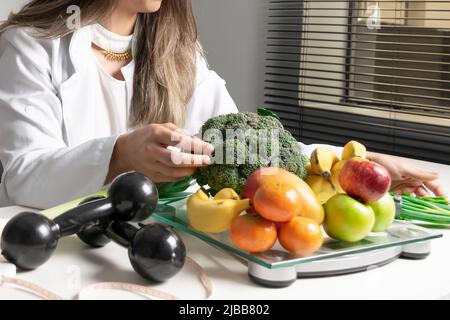 Nutrizionista femminile nel suo ufficio, mostrando verdure e frutta sane. Concetto di salute e dieta. Stile di vita. Foto Stock