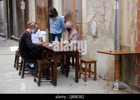 Quattro uomini, indossare maschere, giocare a gioco di domino a tavola in legno nella strada della città vecchia, Coimbra, Portogallo Foto Stock