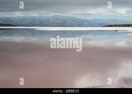 L'acqua negli stagni di evaporazione del sale utilizzati per la raccolta del sale marino dall'oceano Pacifico riflette il cielo nuvoloso coperto. Foto Stock