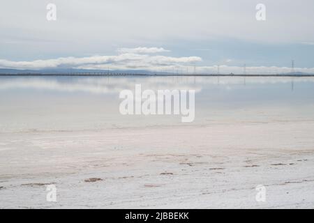 L'acqua mirrorlike glassy di evaporazione del sale stagni che riflettono le nuvole e le linee elettriche. Foto Stock