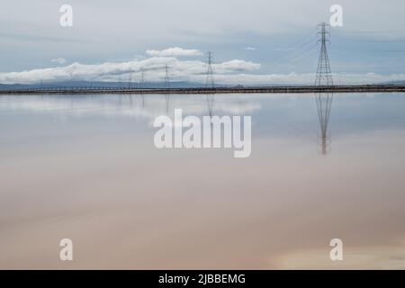 L'acqua mirrorlike glassy di evaporazione del sale stagni che riflettono le nuvole e le linee elettriche. Foto Stock