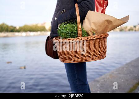 Donna in piedi alla riva del fiume Moldava a Praga con un cestino di microgrene e generi alimentari dal mercato agricolo di Naplavka Foto Stock