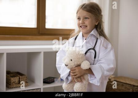 Bambina indossare cappotto bianco tiene ripieno giocattolo gioco medico Foto Stock