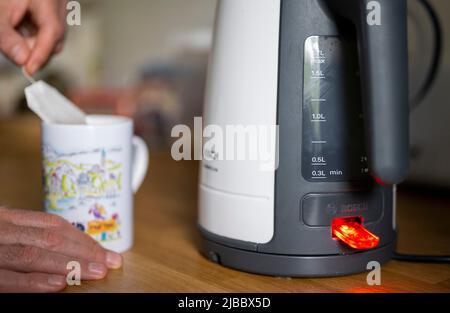 Berlino, Germania. 04th giugno 2022. L'acqua bolle in un bollitore elettrico mentre sullo sfondo un uomo mette una bustina di tè in una tazza. Credit: Monika Skolimowska/dpa/Alamy Live News Foto Stock