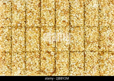 Primo piano con tostatura al sesamo. Caramelle da semi di sesamo. Semi di sesamo tostati bianchi in caramello, kozinaki fresco Foto Stock