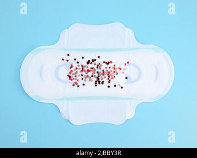 Un pad mestruale con glitter rossa su sfondo blu. Prodotto per l'igiene femminile per la protezione dei giorni di sanguinamento mestruale. Ciclo mestruale Foto Stock