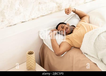 Joyful Arabic Man Awakening Stretching Arms Lying in Bedroom Indoor Foto Stock