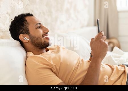 Allegro uomo arabo ascolto di musica con smartphone in camera da letto Foto Stock