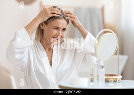 Donna di mezza età turbata che controlla i suoi capelli Foto Stock