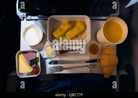 formaggi verdure frittata di pane e altri cibi sul tavolo pieghevole durante il volo in aereo di notte. Foto Stock