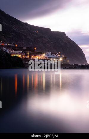 Porto Moniz, Madeira, Portogallo - si riflette in un mare liscio. Lunga esposizione con le luci della città che si riflettono sul paesaggio marino Foto Stock