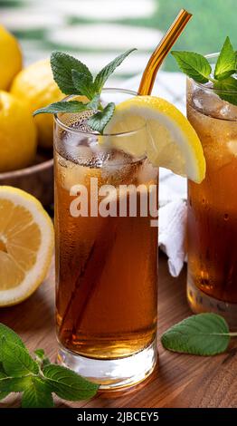 Bicchiere di tè freddo con fetta di limone, menta e cubetti di ghiaccio su tavola di legno Foto Stock
