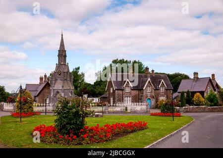 Village Green e case in pietra tagliate di Ardagh, Irlanda, con una torre dell'orologio in stile gotico indipendente. Foto Stock