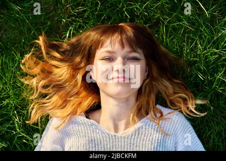 Primo piano volto di felice redhead teenage femmina su sfondo erboso, vista dall'alto Foto Stock