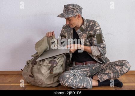 Soldato occupato con zaino utilizzando un portatile militare Foto Stock