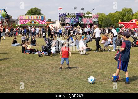 I bambini che giocano nel parco in un fine settimana soleggiato di festa della banca, con una fiera sullo sfondo in estate, Newmarket, Suffolk UK Foto Stock
