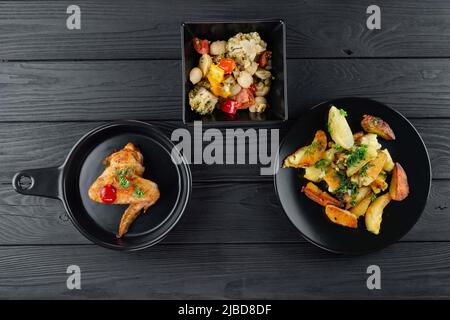 Patate fritte con funghi e pomodori su sfondo nero con spezie. Deliziose patate con verdure e spezie con pollo fritto in un bl Foto Stock