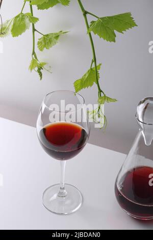 Un bicchiere di vino rosso e un decanter su un tavolo bianco. Sfondo chiaro. Foto Stock