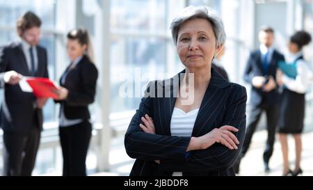 Ritratto di donna d'affari asiatica matura in carica con le braccia incrociate e sorridenti. Dirigente asiatico femminile che guarda la fotocamera con sicurezza. Foto Stock