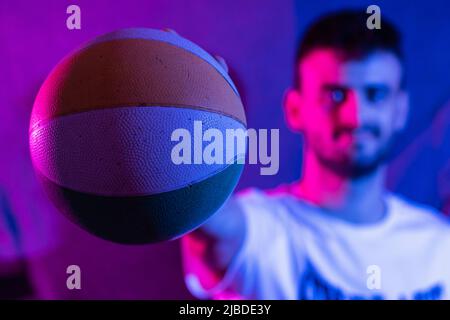 Un giovane uomo caucasico con braccio allungato che tiene una piccola basket di vari colori. La palla è a fuoco in primo piano e il perso Foto Stock