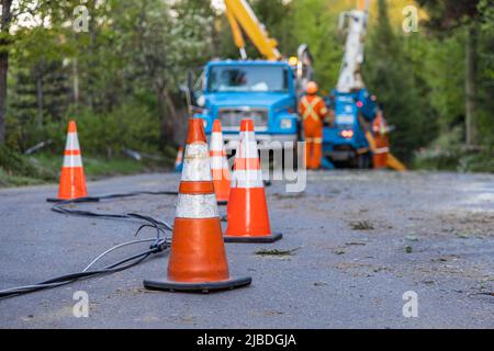 Vista selettiva dei coni stradali ad alta visibilità che avvisano il traffico della caduta della linea elettrica aerea dopo la tempesta. Gli appaltatori poco nitidi lavorano per ripristinare l'elettricità. Foto Stock