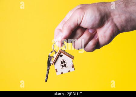 Acquisto di una casa. L'acquirente riceve la chiave per la proprietà. Appartamento ipotecario. Chiavi e una piccola casa in legno in mano. Consegna delle chiavi all'Ora Foto Stock