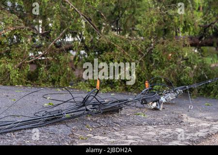 Primo piano fuoco selettivo di pericolosi cavi di alimentazione elettrica che giacciono su asfalto della strada principale dopo che i venti alti abbassano le linee elettriche aeree. Foto Stock