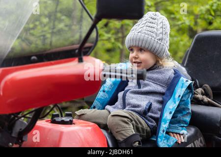 Ritratto candido con fuoco selettivo su un ragazzo felice di quattro anni seduto slumped indietro nel sedile di guida di una moto quad. Copia spazio su lato. Foto Stock