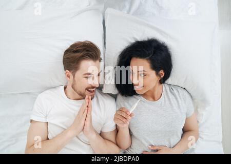 Coppia sdraiata a letto gioendo alla notizia del futuro bambino Foto Stock