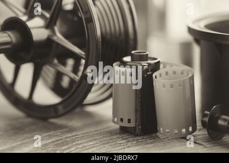 Rotolo e cassetta di pellicola fotografica, attrezzatura fotografica - vasca di sviluppo con le sue bobine di pellicola su sfondo. Messa a fuoco selettiva. Foto retrò in bianco e nero Foto Stock