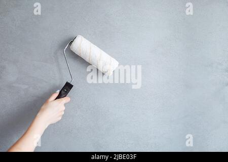 Immagine ritagliata di una mano che tiene un rullo di pittura mentre dipingi una parete della casa. Foto Stock