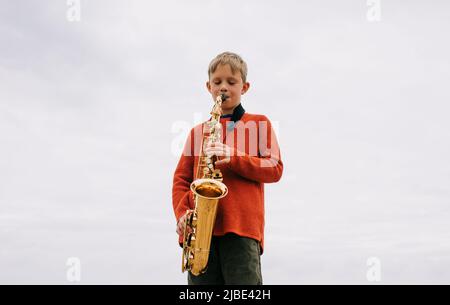 ragazzo felice di giocare il sassofono all'aperto Foto Stock