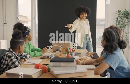 Classe con diversi studenti di studenti felicemente afroamericani e insegnanti che svolgono attività insieme. L'insegnante sta insegnando, guidando e talki Foto Stock