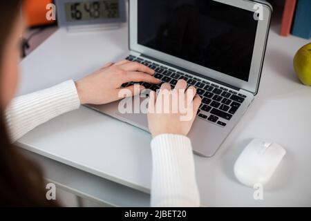 Alla sua scrivania, una ragazza digita rapidamente un messaggio sulla tastiera del suo laptop. Foto Stock