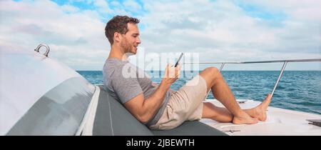 Telefono in uso sulla nave da crociera. Uomo viaggi di lusso SMS con dati su barca barca relax sul ponte banner panoramico. Vacanze Caraibi Foto Stock