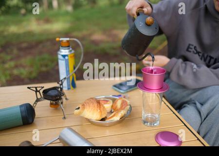 Caffè gocciolare mentre campeggio in foresta con il sole. Macchina per il caffè all'aperto, campeggio stile di vita picnic mattina, persona che cucinano una bevanda calda in campeggio natura Foto Stock