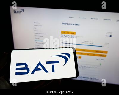 Persona che tiene il telefono cellulare con il logo della società British American Tobacco plc (BAT) sullo schermo di fronte alla pagina web. Mettere a fuoco sul display del telefono. Foto Stock