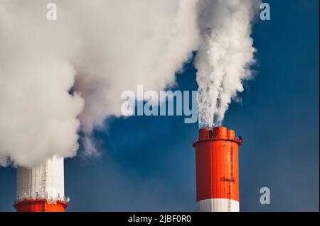 Pesanti nubi di vapore bianco si innalzano su camini di pianta Foto Stock