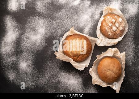 Prodotti da forno freschi, pane rustico croccante e panini su sfondo di pietra nera con farina, cottura fatta in casa, vista dall'alto, piatto Foto Stock