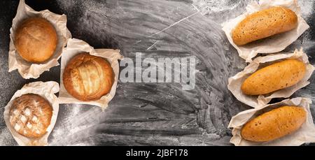 Assortimento di vari deliziosi pane appena sfornato, su sfondo di cemento nero con spazio copia vista dall'alto della farina, panetteria e cibi sani Foto Stock