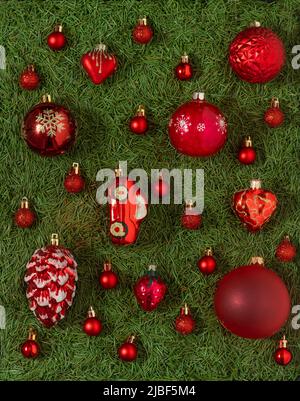 Un set di diversi giocattoli rossi di Natale su uno sfondo verde di aghi dell'albero di Natale. Palla rossa. Decorazioni e decorazioni. Concetto di anno nuovo. Foto Stock