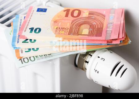 Pila di banconote in euro sulla batteria del radiatore di riscaldamento con termostato regolatore di temperatura. Concetto di costi di riscaldamento costosi ed energia in aumento Foto Stock