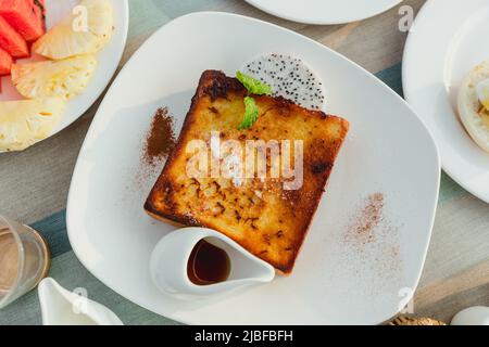 toast alla francese su un piatto bianco con cannella circondato da un piatto di frutta Foto Stock