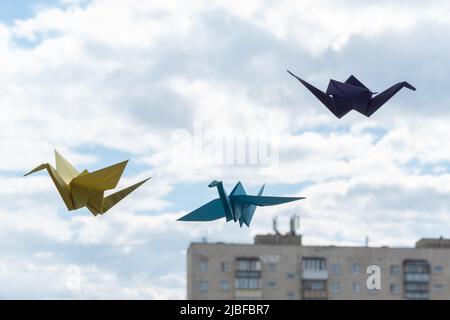 Autogru di uccelli di origami di carta multicolore appese alla finestra sullo sfondo del cielo. Origami gru in stile giapponese è un simbolo di happine Foto Stock